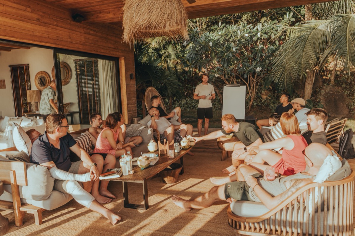 Fabian Ries steht vor einer Gruppe auf einer überdachten Terrasse auf Koh Phangan, die Teilnehmer sitzen auf Sofas und hören zu